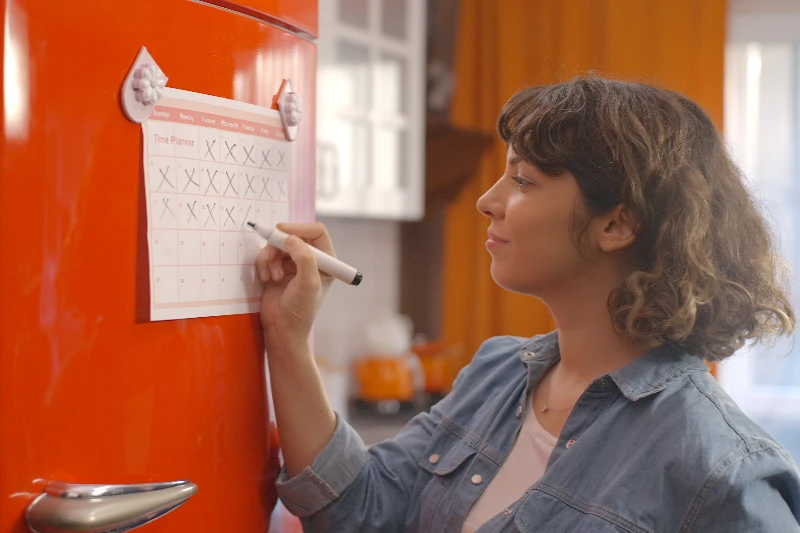 Blog 7 Woman marking off her calendar hanging on a fridge
